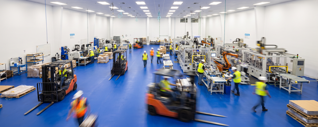 Active manufacturing facility with a blue floor, workers, and forklifts